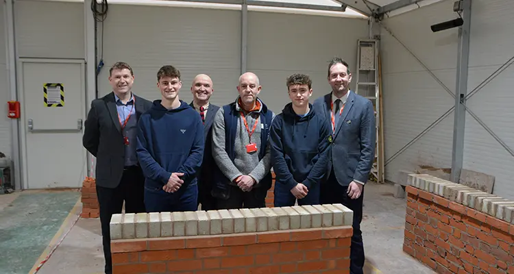 A group of students and staff standing in front of small brick wall