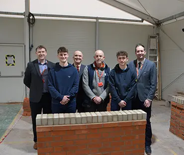 A group of students and staff standing in front of small brick wall