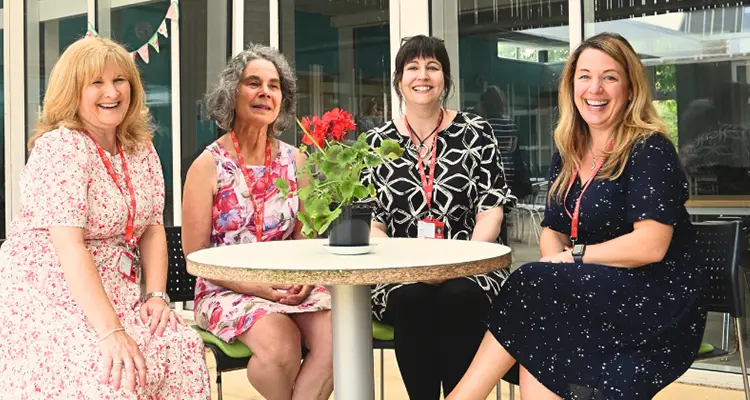 Four higher education teachers smiling, sat around a table in courtyard