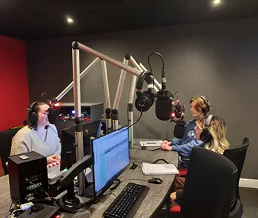 Students in a podcast room, talking into microphones