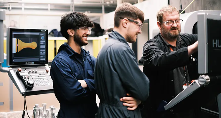 Two engineering students working on machinery with teacher