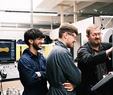 Two engineering students working on machinery with teacher